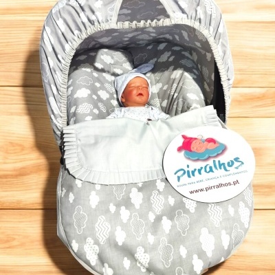 Saco-cama para bebé cinzento com padrão de nuvens brancas, boneco bebê dentro e etiqueta Pirralhos
