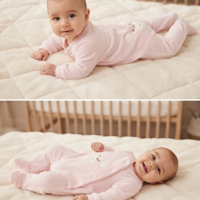 Bebé em pijama rosa com ursinho numa cama branca acolchoada