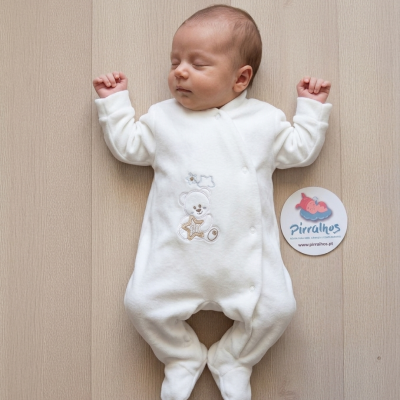 Macacão branco para bebé com ursinho bordado e estrela-do-mar, em fundo de madeira clara, com etiqueta redonda ao lado