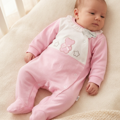 Bebé com macacão cor-de-rosa e branco com ursinho e estrelas, deitado numa manta creme texturizada