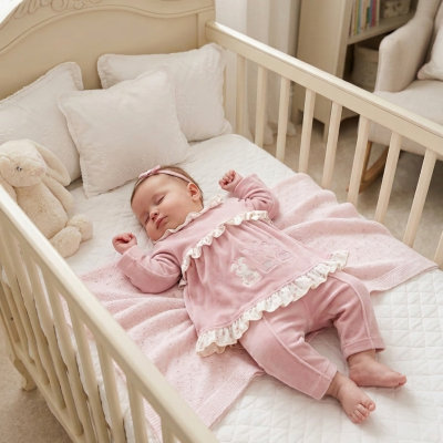 Bebé a dormir num berço branco com roupa rosa e brinquedo de pelúcia coelho