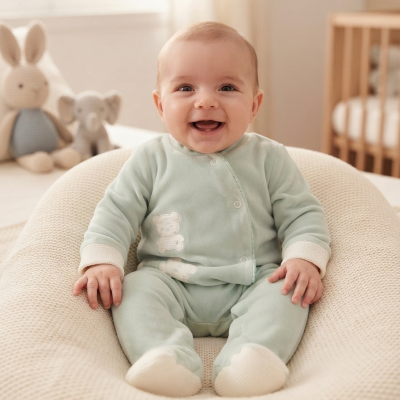 Bebé sorridente em pijama verde num suporte almofadado bege