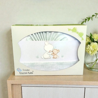 Conjunto para bebé branco e cinza claro com bordado de coelhinhos em caixa decorada verde sobre móvel de madeira
