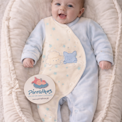 Bebé de macacão azul claro e creme com desenhos, deitado em suporte acolchoado creme com laço
