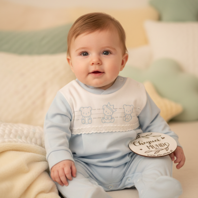 Bebé sentado com roupa azul claro e branca decorada com ursinhos e chapa de madeira