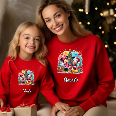 Duas pessoas com sweats vermelhas da Disney com nomes personalizados, ao lado de presentes e árvore de Natal.
