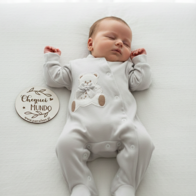 Bebé dormindo com pijama cinza claro com urso bordado e círculo de madeira com texto ao lado
