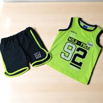 Conjunto de roupa infantil verde e preta com texto e números, sobre superfície de madeira clara