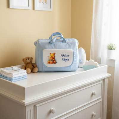 Bolsa para bebé azul com urso e nome Vasco Elgar sobre cómoda branca num quarto infantil