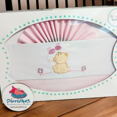 Conjunto de roupa de bebé rosa e branco com bordado de urso, em caixa branca com estrelas azuis