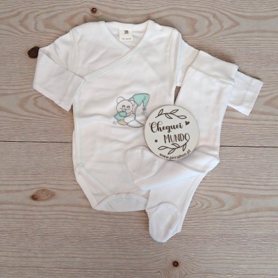 Conjunto branco para bebé com bordado de ursinho e lua, etiqueta com texto sobre madeira clara