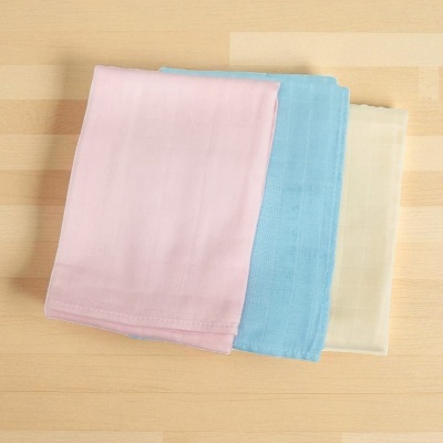 Três panos dobrados em tecido liso de cores pastel sobre madeira clara