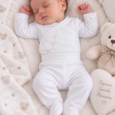 Bebé dormindo vestido com conjunto branco e manta com padrão de ursos.