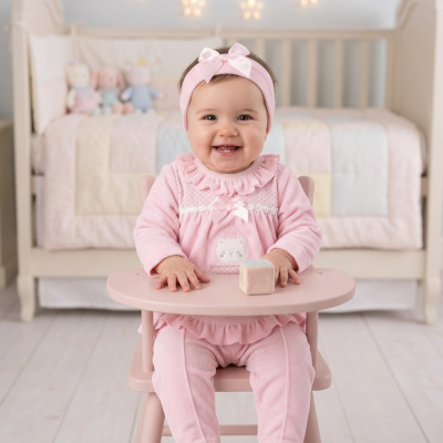Bebé sorridente sentada numa cadeira alta rosa em quarto de bebé decorado