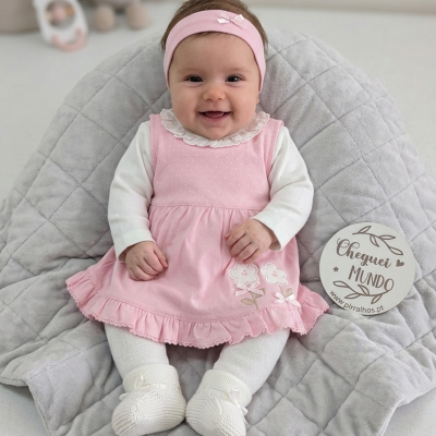 bebé com vestido rosa sentado sobre manta cinzenta acolchoada