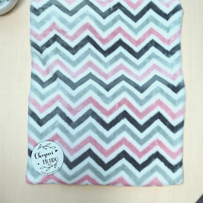 Cobertor ou manta com padrão ziguezague cinza, rosa e branco sobre uma mesa clara