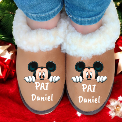 Chinelos marrons com pelo branco e desenho do Mickey Mouse, texto 'PAI Daniel', usados por pessoa com calças de ganga, fundo vermelho de Natal