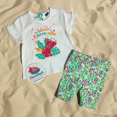 Conjunto roupa infantil com t-shirt branca e calções florais sobre areia