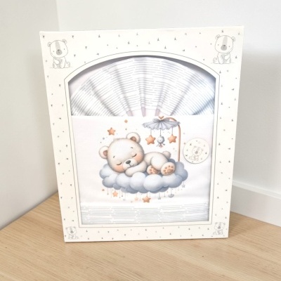 Caixa branca com padrão e desenho de urso e roupa de bebé com urso a dormir na nuvem.