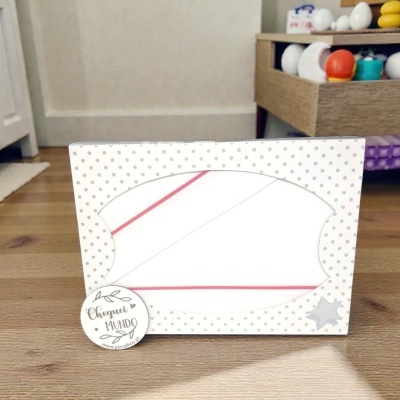 Caixa branca com padrão de bolinhas cinzentas, texto Cheguei MUNDO em peça redonda