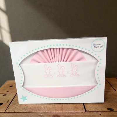 Roupa de bebé rosa e branca com bordado de coelhinhos numa caixa branca com estrelas.