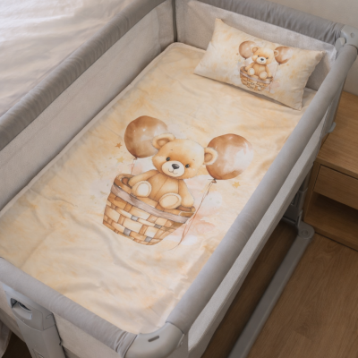 Berço portátil cinzento com colcha e almofada bege com desenho de urso castanho