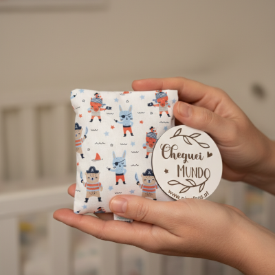 Almofada pequena com padrão de piratas coloridos e etiqueta Cheguei MUNDO, mãos segurando