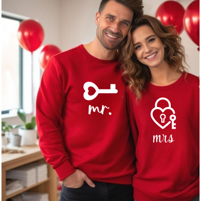 Casal com camisolas vermelhas 'mr.' e 'mrs.' com chave e cadeado em ambiente com balões vermelhos