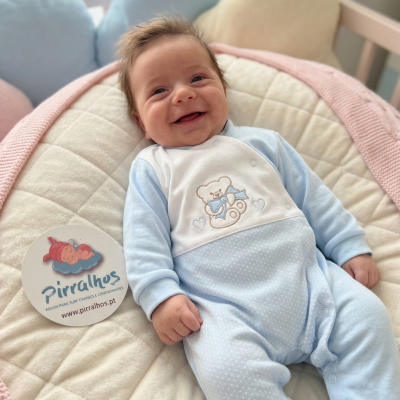 Bebé sorridente com babygrow azul claro e branco com bordado de ursinho.