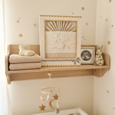 Prateleira com roupa de bebé bege, quadro bordado com coelhos, ecografia e decoração de coelho num quarto de bebé
