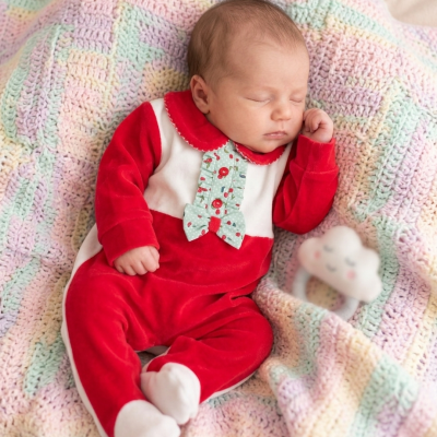 Bebé a dormir com fato vermelho e branco sobre manta crochet pastel com brinquedo nuvem