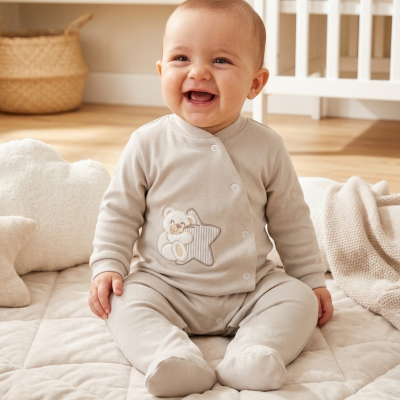 Bebé sorridente vestido com macacão bege claro sentado em tapete acolchoado bege num quarto de bebé