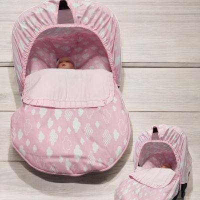 Carrinho de bebé rosa com padrão branco de nuvens e capota em fundo de madeira clara