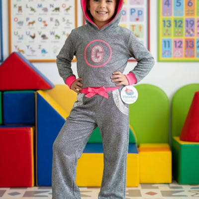 Menina com fato cinzento com capuz e letras rosa num ambiente colorido educativo