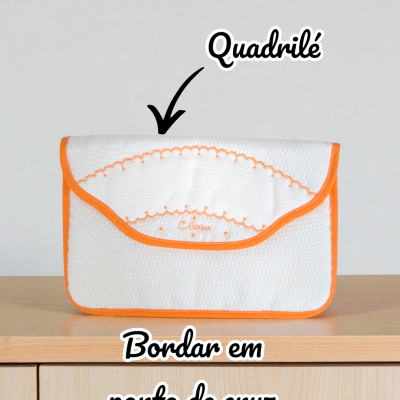 Bolsa branca com bordado laranja e borda laranja, sobre móvel de madeira clara