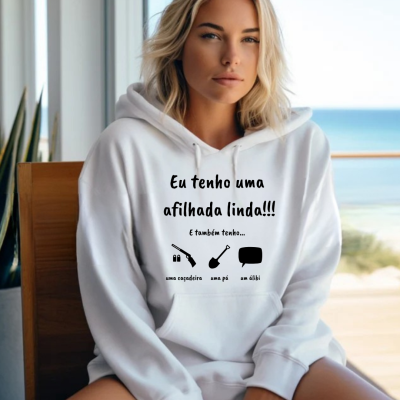 Mulher a usar casaco branco com capuz com texto em português e ícones, sentada em cadeira junto a uma janela com vista para o mar.