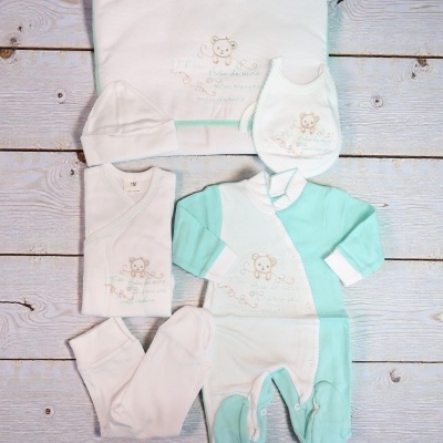 Conjunto de roupa de bebê branco e verde-água com bordado de ursinho sobre madeira clara
