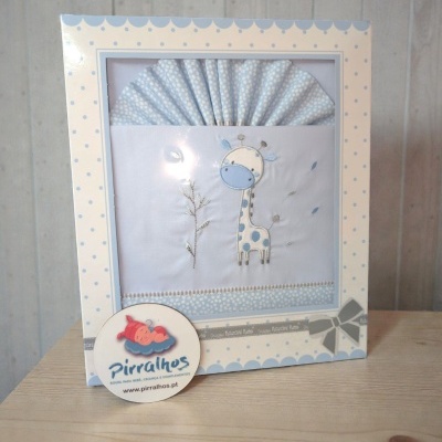 Fralda de bebé branca com bordado de girafa azul e bege numa caixa decorada com bolinhas azuis e bege.