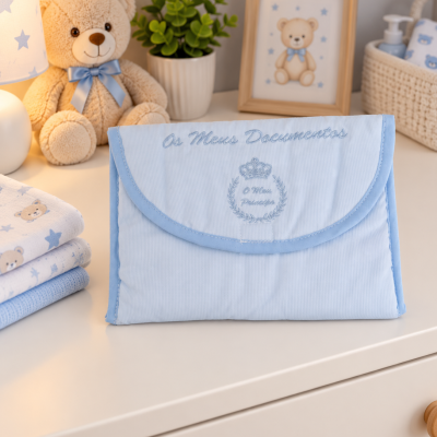 Bolsa azul clara para documentos de bebé com bordado em tom azul, em ambiente de quarto infantil com ursinho de peluche e fraldas.
