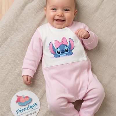 bebé sorridente com macacão rosa e branco com estampa de personagem azul e laço rosa deitado em tecido bege