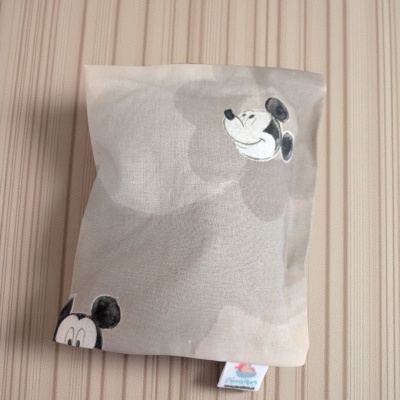 Almofada cinza clara com estampas do rosto do Mickey Mouse em preto e branco sobre superfície de madeira clara.