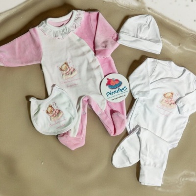 Conjunto de roupa de bebé rosa e branco com estampas de ursinhos sobre fundo bege texturizado