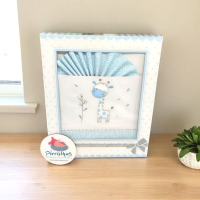 Conjunto de roupa de bebé azul com girafa bordada numa caixa decorativa com padrão de pontos azuis.