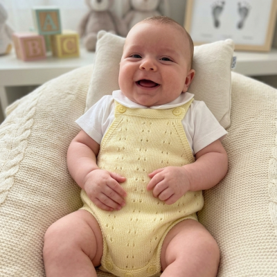 Bebé sorridente em roupa de malha amarela sentado em almofada creme com fundo difuso