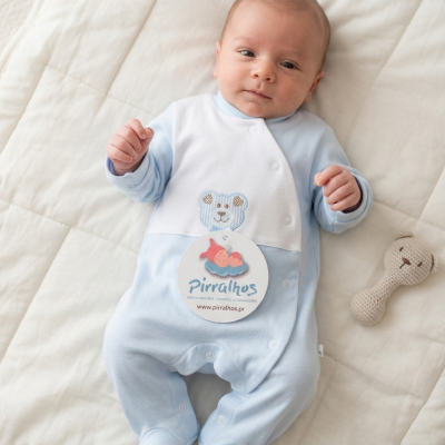 Fato de bebé azul claro com ursinho bordado e etiqueta Pirralhos num fundo branco macio, com brinquedo de malha ao lado.