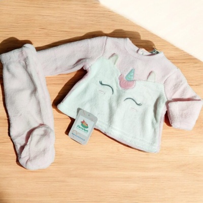 Conjunto bebé rosa unicórnio em tecido felpudo sobre mesa de madeira
