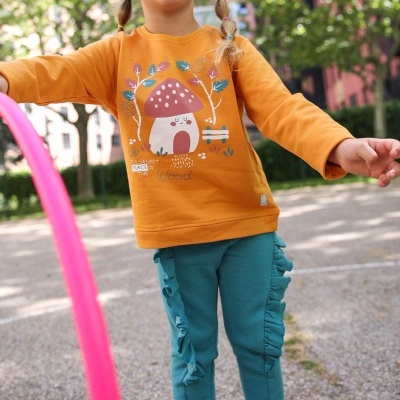Criança com camisola laranja e calças azuis jogando em parque exterior