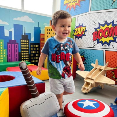 Criança com t-shirt de heróis e brinquedos temáticos em sala colorida