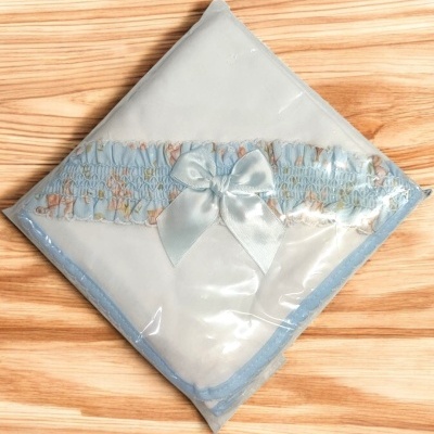 Manta branca para bebé com contorno e laço azul clara, embalada em plástico