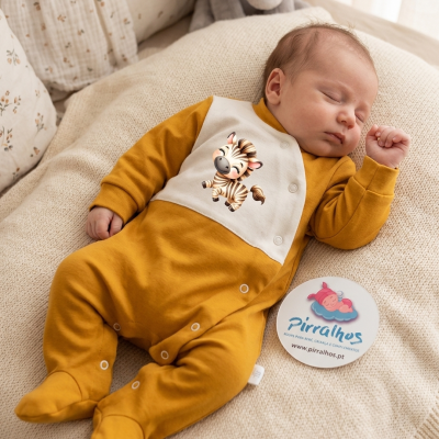 Bebé dormindo com pijama mostarda e bege com estampa de zebra, deitado numa manta beige com cartão com marca Pirralhos ao lado.